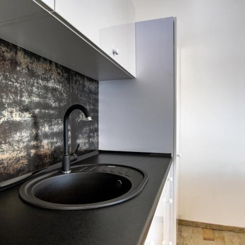 interior-of-modern-spacious-kitchen-with-white-contemporary-furniture-black-ceramic-tiles-on-the-wall-and-dark-granite-sink-with-water-tap-min